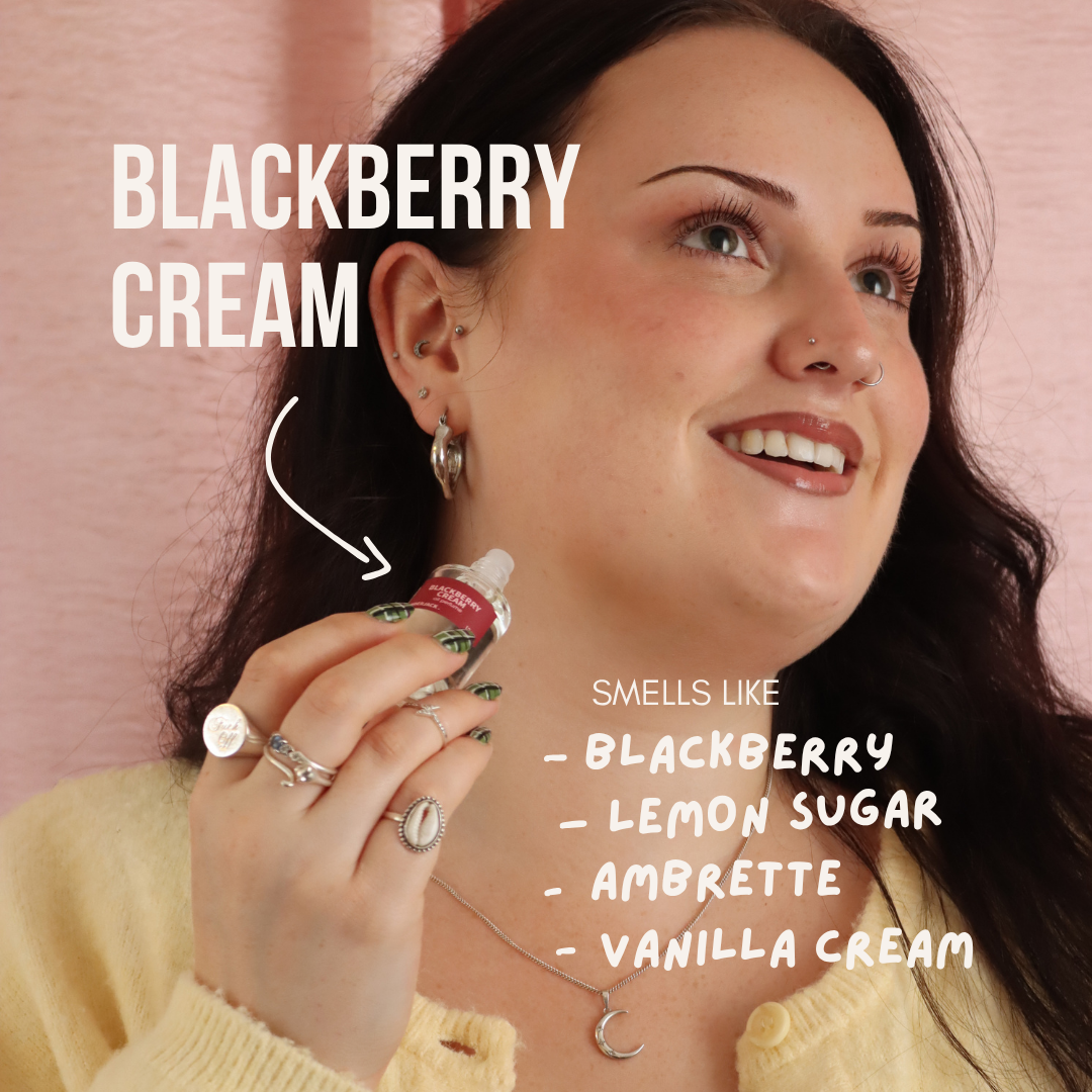 Smiling woman holding a small Blackberry Cream perfume oil roll-on with a white cap.