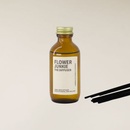 Amber glass "Flower Junkie" reed diffuser bottle with gold cap and black reeds on a light background.