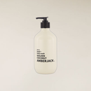 A frosted white pump bottle of hand and body wash with a black dispenser, labeled 'AMBERJACK' and 'GOLDEN COCONUT', centered against a solid light beige background.