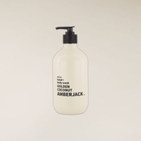 A frosted white pump bottle of hand and body wash with a black dispenser, labeled 'AMBERJACK' and 'GOLDEN COCONUT', centered against a solid light beige background.