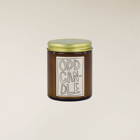 Brown glass Odd Candle with a gold lid and a white label featuring hand-drawn text.