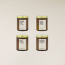 Four amber glass soy candles with gold lids and white labels, featuring different fragrance names.