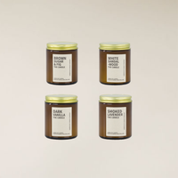 Four amber glass soy candles with gold lids and white labels, featuring different fragrance names.