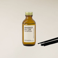 Amber brown glass "Whiskey in a Jar" reed diffuser with gold cap and black reed sticks.